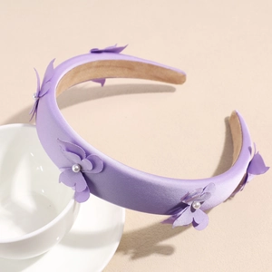 Detail of purple satin bow headband featuring elegant pearls on a soft cream background
