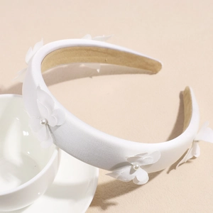 Detailed view of white satin bow headband with decorative fabric flowers and pearls