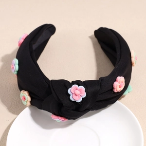 Détail d'un serre-tête noir noué avec des fleurs 3D en résine colorées sur une assiette