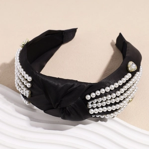 Detail of black satin headband with knotted top, white pearls and heart rhinestones