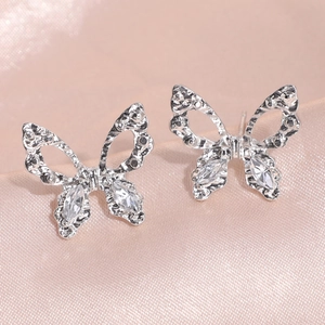 Detalle de pendientes de mariposa con alas de metal y circonitas sobre seda rosa suave