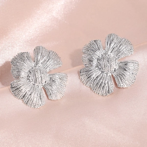 Primer plano de aretes de flores plateadas con textura de cinco pétalos sobre seda rosa