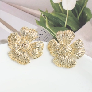 Detalle de pendientes de flores doradas con acabado texturizado en un plato de porcelana