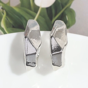 Primer plano de pendientes de plata con textura de metal fundido y acabado espejo