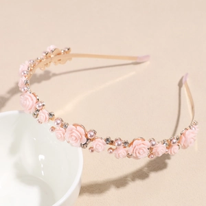 Détail des roses en résine rose et des perles sur un serre-tête floral doré chic