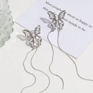Detalle de pendientes de mariposa con borla plateada, circón y perla en fondo blanco