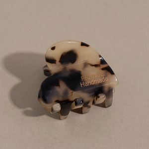 Close-up of tortoise shell heart hair claw with gold France Handmade logo on beige surface