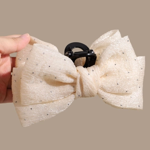 Detail of a beige mesh bow hair claw clip with silver rhinestones and black grip