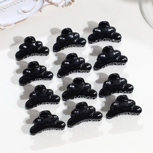 Set di 12 mini mollette nere lucide a forma di corona per capelli su fondo crema chiaro