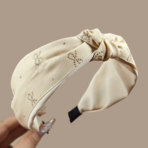 Détail d'un serre-tête beige avec nœuds en strass brillants et design noué sur le dessus