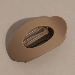 Détail macro d'une grande pince à cheveux ovale marron mate au design épuré creux