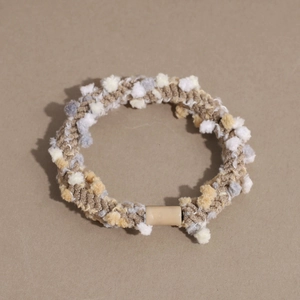 Close-up of woven hair tie with soft pom-poms and durable cylindrical resin fastener