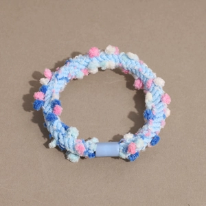 Detail of blue knitted hair tie featuring colorful pom-poms and smooth plastic joint