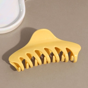 Gros plan d'une grande pince à cheveux jaune vif sur un fond gris texturé minimaliste