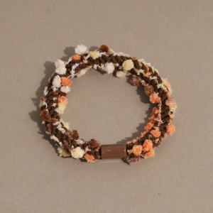 Detail of multi-color knitted elastic hair tie with textured pom-poms and brown joiner