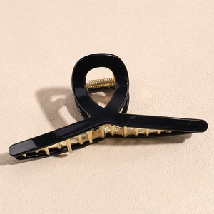 Detail of a large black acrylic hair claw with cross ring design and gold metal spring