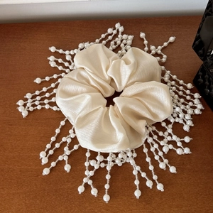 Macro detail of French silk scrunchie featuring elegant white pearl tassels on wood