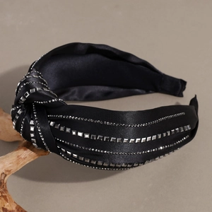 Close-up of black satin knotted headband featuring rows of silver rhinestones and metal studs
