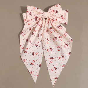 Close-up of fabric bow hair clip featuring Santa Claus prints and long decorative ribbons