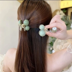 Detail view of light green spherical hair claw clips on long hair with a side-angle view