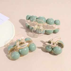 Three sizes of mint green acrylic claw clips with gold metal springs on beige background