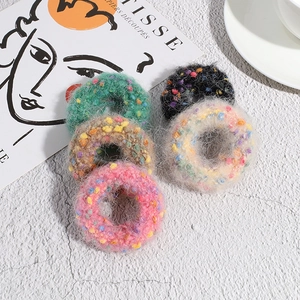 Five colorful knitted polka dot hair scrunchies displayed on a minimalist art book background