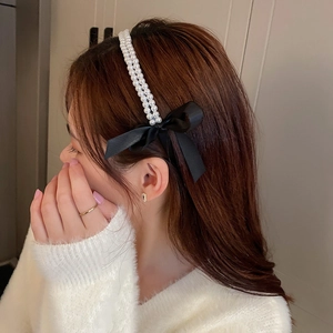 Close-up of dual-row pearl headband with a black satin bow on model with soft lighting