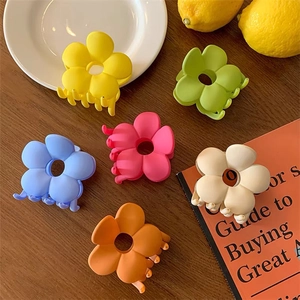 Close-up of matte flower hair claws in six vibrant colors on a wooden surface