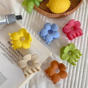 Detailed view of six colorful matte flower hair claws on a clean fabric background