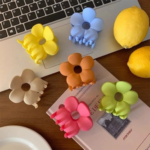 Flat lay of six matte flower hair claws in assorted pastel colors on a desktop background