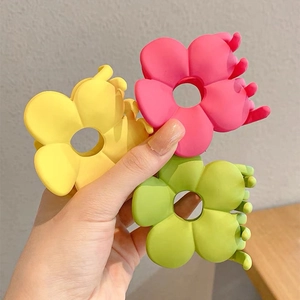 Detailed macro of three matte flower hair claws in yellow, pink, and green colors