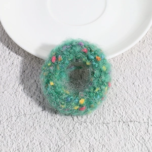 Detailed knit texture of green polka dot hair tie with colorful plush accents on ceramic plate