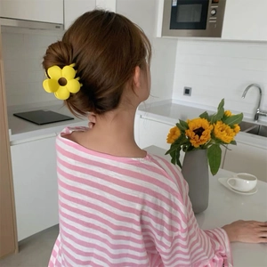 Detail view of a yellow flower-shaped hair claw clip used in an elegant bun hairstyle