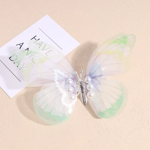 Détail d'une pince à cheveux papillon mobile avec ailes vertes et perles blanches