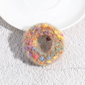 Macro detail of plush brown knit scrunchie featuring colorful polka dot pom-pom accents