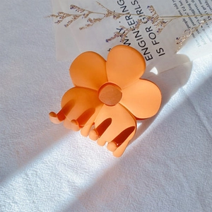 Detail shot of a matte orange flower hair claw clip on a stylish fabric background