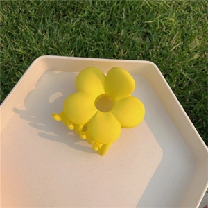 Close-up of yellow flower hair claw clip with matte finish on a white plate over grass