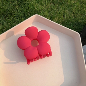 Close-up of a matte rose red flower hair claw clip on a white tray over green grass