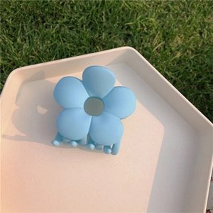 Macro view of light blue flower hair claw clip on a white tray with grass background