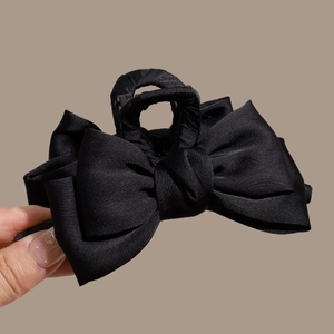 Close-up of a large black satin bow claw clip held in hand to show size and texture