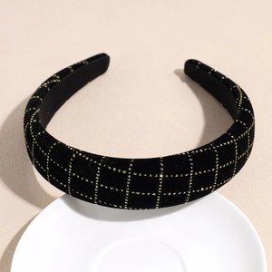 Détail d'un serre-tête en velours noir avec motif quadrillé doré sur assiette blanche