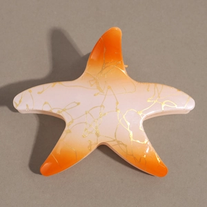 Détail de la pince à cheveux étoile de mer avec dégradé orange et texture dorée