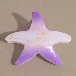 Détail macro d'une pince à cheveux étoile de mer avec dégradé violet et motifs dorés