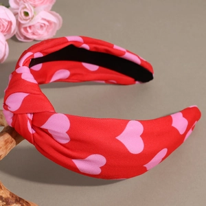 Dettaglio del cerchietto annodato in tessuto rosso con cuori rosa su supporto