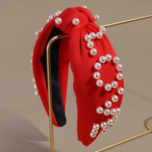 Close-up of red knotted headband featuring white pearl letter patterns on a gold display