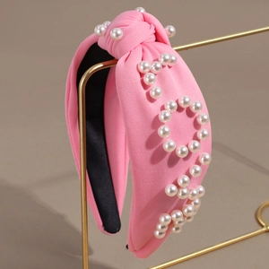 Elegant pink fabric knotted headband with pearl letter embellishments on a gold stand