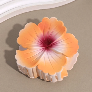 Detail view of a frosted gradient frangipani flower hair claw clip with orange-pink petals