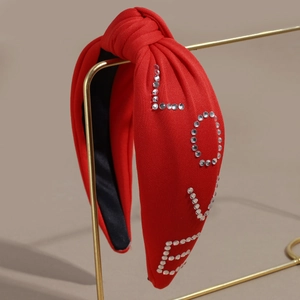 Detailed close-up of red knitted headband with rhinestone LOVE letters on gold stand