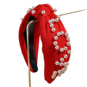 Elegant red textured fabric knotted headband with white pearls on a gold metal stand