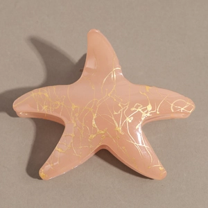 Détail de la pince à cheveux étoile de mer rose avec motifs de texture sable doré